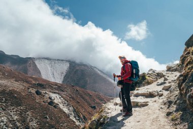 Bulutlarda gezinen yürüyüşçü silueti Imja Khola vadisinde ayakta duruyor ve Tengboche yakınlarındaki Everest Kampı yürüyüş rotasında dağ manzarasının keyfini çıkarıyor. Etkin tatil resmi