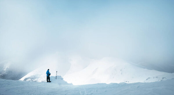 Winter Trekker staying on mountain peak he climbed and enjojing wide panorame view of valley covered by storm clouds. Active winter trekking concept image.