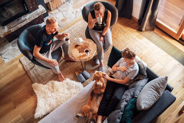 Cozy family tea time. Father, mother and son  at the home living room. Boy lying in comfortable sofa and  stroking their beagle dog and smiling. Peaceful family moments concept image.