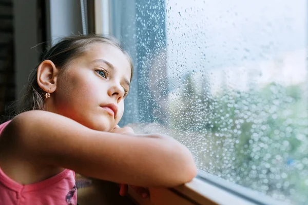 小女孩忧心忡忡地望着窗玻璃里的雨滴很多 悲伤童年的概念形象 — 图库照片