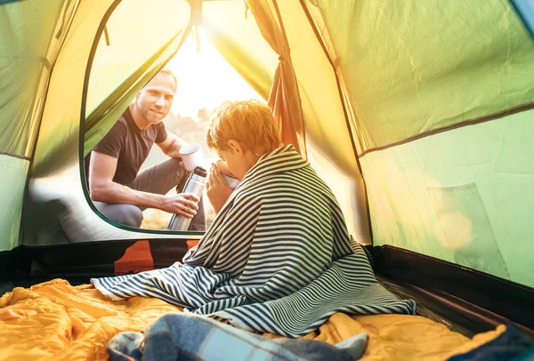 Tea break in camp tent: father and son drink hot tea at evening time