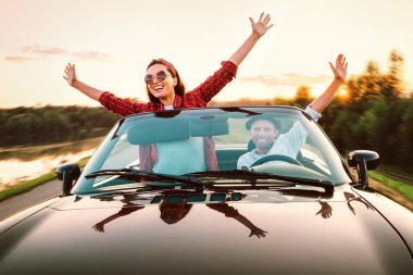 Arabayla seyahat etmek - aşık mutlu bir çift gün batımında Cabriolet arabasıyla gider