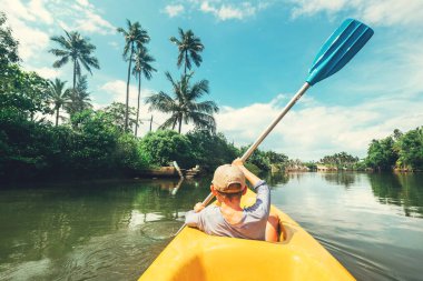 Çocuk tropikal gölde kano teknesinde yelken açıyor.