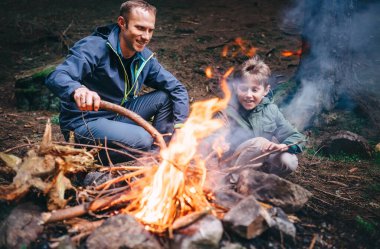 Baba ve oğul ormanda şenlik ateşi yakıyor. İlkbaharda ya da sonbaharda kamp gezisi