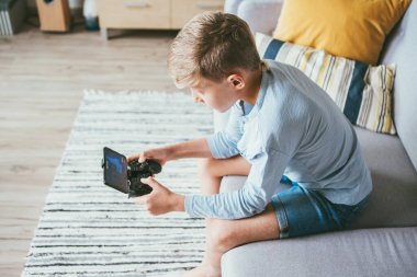 Çocuk bilgisayar oyununda kayboldu. Evde kanepede oturuyor, akıllı telefonlu oyun sahası kullanıyor. Çocuk elektronik aygıt kullanımı kavramı