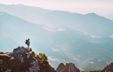 Sırt çantalı dağ yürüyüşçüsü küçük heykelcik nefes kesici tepeleri olan dağ zirvesinde kalır.