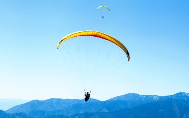 Mavi dağların üzerinde gökyüzünde süzülen iki Paraglider 