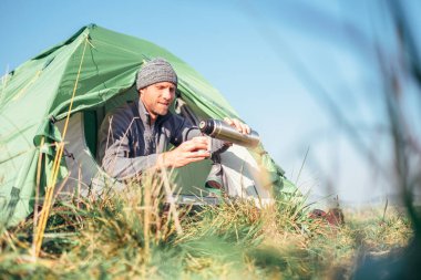 Adam çadırda oturur ve sıcak çay içer. 