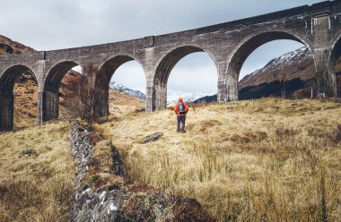 Yürüyüş, sırt çantasıyla yürümek, aktif yaşam tarzı konsept görüntüsü. Erkek gezgin İskoçya 'daki ünlü Glenfinnan Viadukt' un yanında yürüyor.