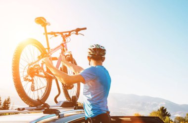 Dağ bisikletçisi. Motosikletini arabanın çatısından al. Akşam üstü görüntüsü.