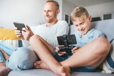 Baba ve oğul, bilgisayar oyuncuları, elektronik cihazlarla hevesle oynuyorlar: tablet ve oyun alanı.