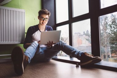 Dizüstü bilgisayarla çalışan öğrenci pencerenin yanında oturuyor.