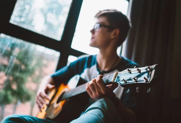 小伙子坐在窗边弹奏吉他 — 图库照片