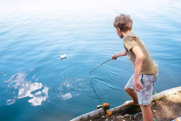 少年は紙ボートで遊び 湖でそれを起動します — ストック写真