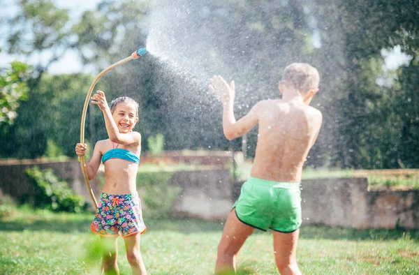 两个孩子 在夏天的花园里玩浇水软管时 玩得很开心 — 图库照片