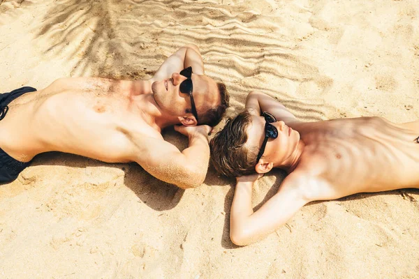父と息子はヤシの木の影に砂の上に横たわっています 熱帯の島の休暇の瞬間 — ストック写真