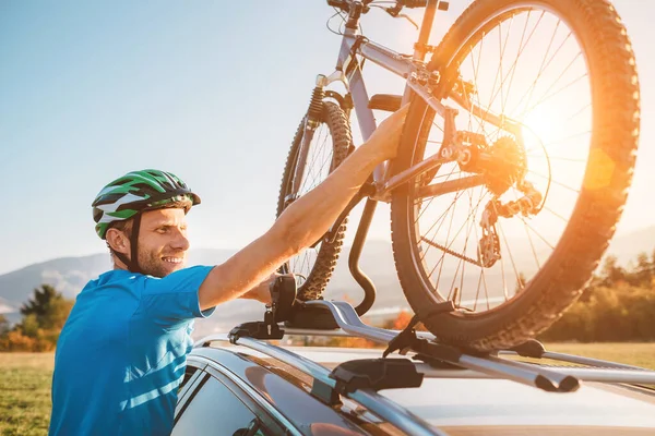 年轻男子身穿自行车服 戴着保护头盔 把他的山地自行车安装在车顶上 — 图库照片