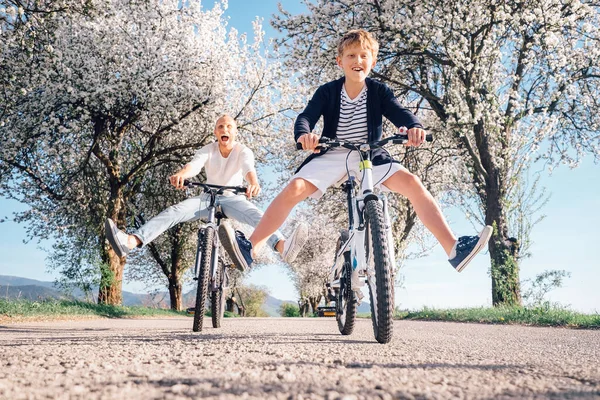 父亲和儿子骑自行车在长满鲜花的乡间路上玩得很开心 — 图库照片
