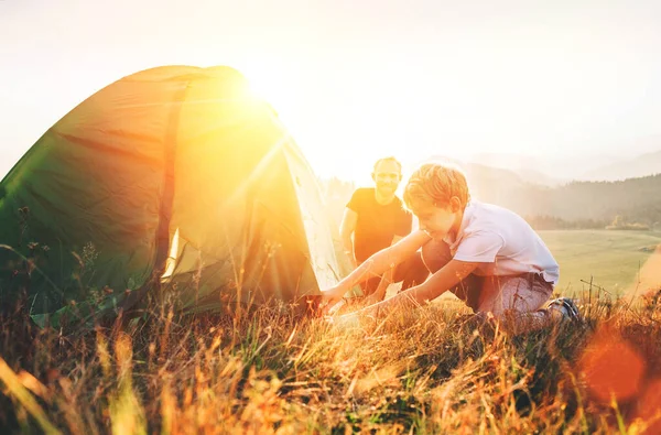 父は日没の森のグレードでキャンプテントを設定彼の息子を学ぶ — ストック写真