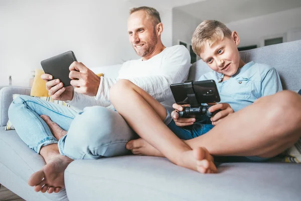 Pai Filho Tocando Entusiasticamente Dispositivos Eletrônicos Tablet Gamepad Sentado Sala — Fotografia de Stock