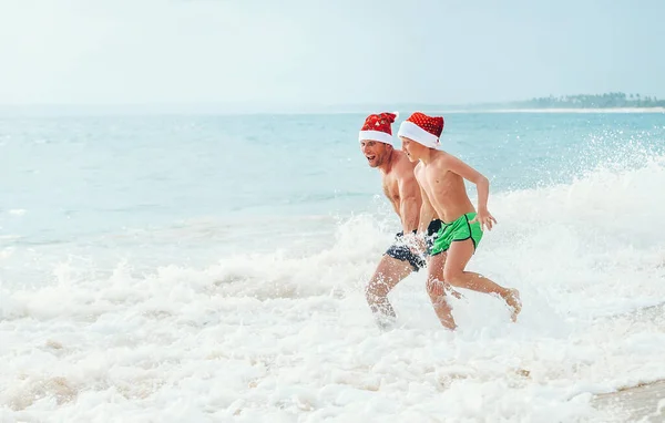 Noel Baba Şapkalı Mutlu Baba Oğul Okyanus Dalgalarında Iyi Eğlenceler — Stok fotoğraf