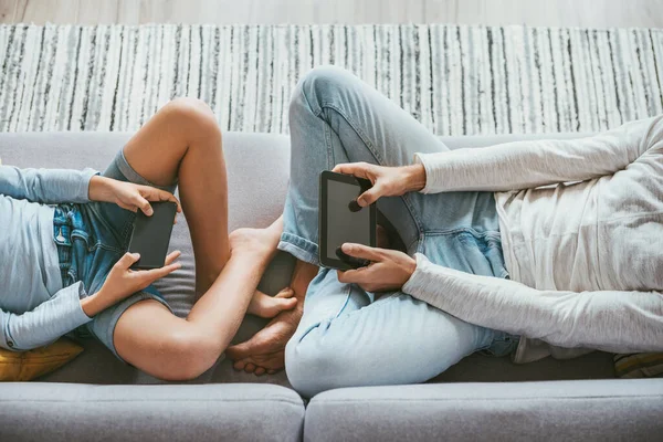 父亲和儿子沉迷于电子设备 两个人坐在沙发上 带着平板电脑和智能手机 手拉手看 — 图库照片