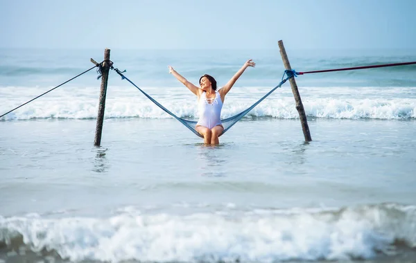美しいです女性楽しみます海の風と太陽座っていますハンモック波の上にスイング — ストック写真