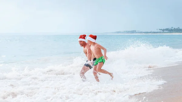 Mutlu Gülümseyen Baba Oğul Noel Baba Şapkalarını Takıp Okyanus Dalgalarında — Stok fotoğraf
