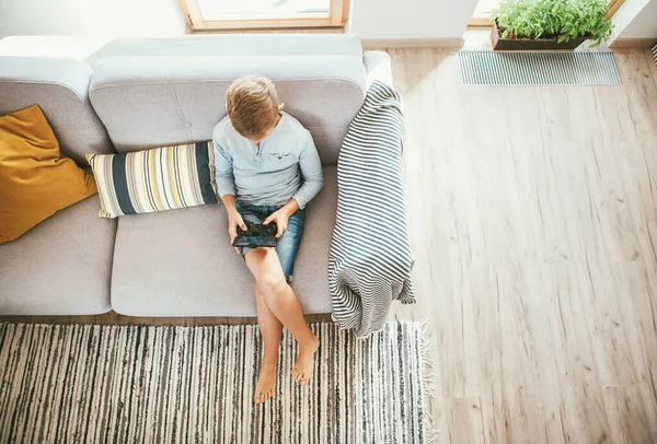 Junge Sitzt Auf Sofa Und Spielt Mit Smartphone Und Gamepad — Stockfoto