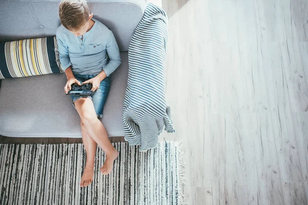 Junge Sitzt Auf Sofa Und Spielt Mit Smartphone Und Gamepad — Stockfoto