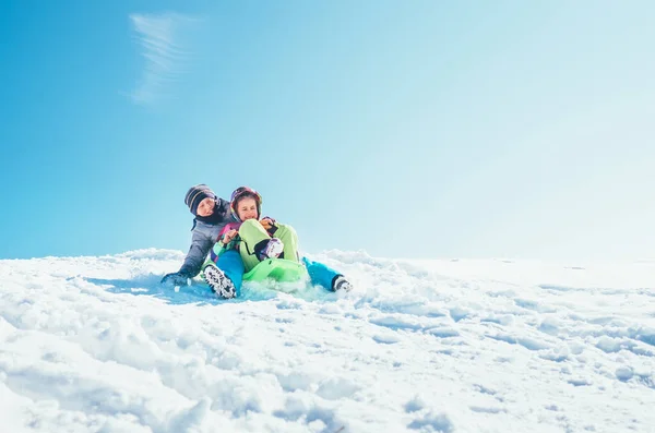 兄弟姉妹の雪の斜面1つのスライドに座ってから下にスライドします 冬のそり時間を楽しむ — ストック写真