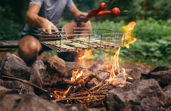 夏のレジャーのコンセプトイメージ 男はキャンプファイヤーで野菜を調理します — ストック写真