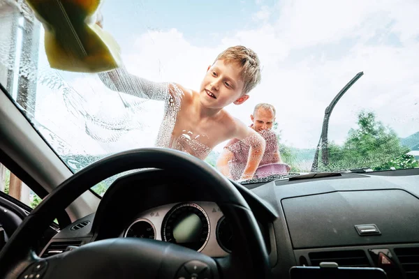 Car washing process: son helps his father to wash a car front window