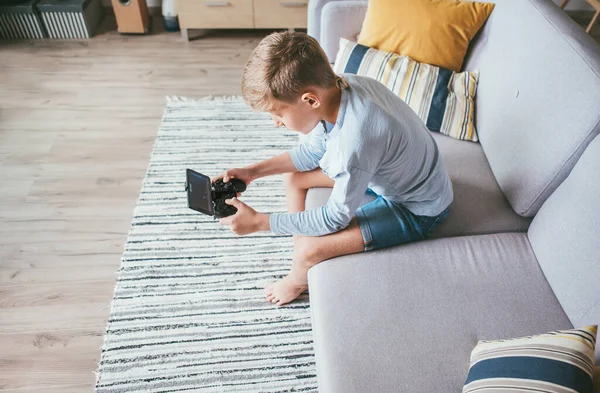 コンピュータゲームで迷子になった18人の少年 居心地の良いソファの上に家に座って スマートフォンでゲームパッドを使用しています トップ表示 — ストック写真