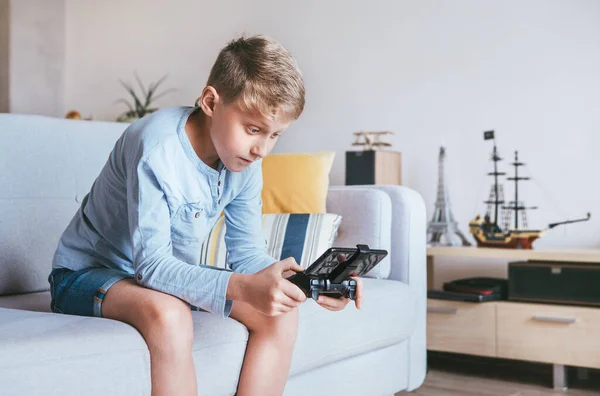 10代の男の子が熱狂的にスマートフォンに接続されたゲームコンソールで再生されます — ストック写真