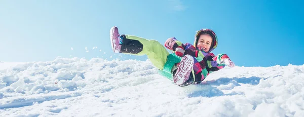 青空を背景に雪の斜面から小さな幸せな女の子のスライドダウン — ストック写真