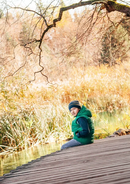 Chlapec Sedí Dřevěném Mostě Podzimního Rybníka — Stock fotografie
