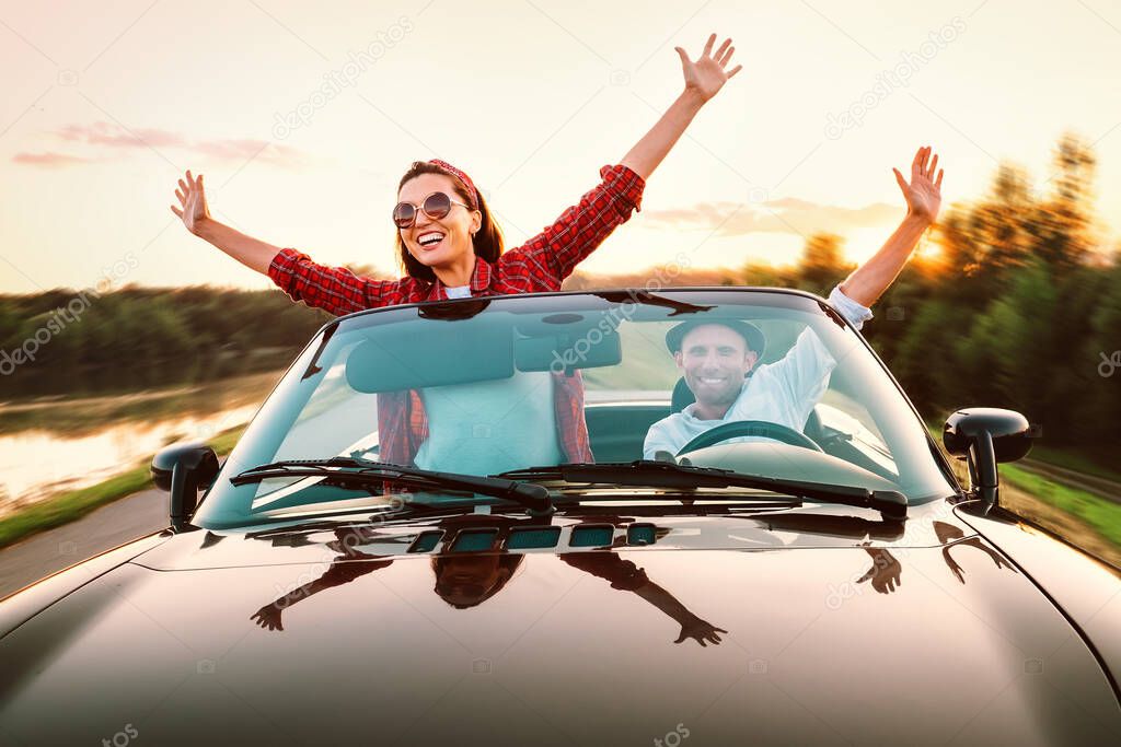 Traveling by car - happy couple in love go by cabriolet car in sunset time