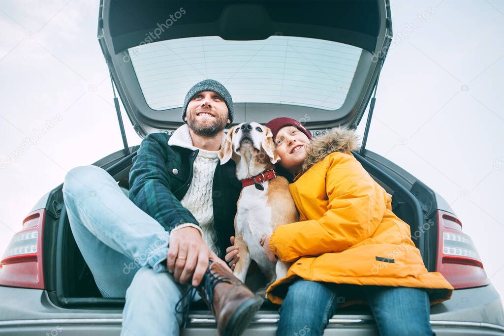 Father and son with beagle dog siting together in car trunk. Long auto journey break.