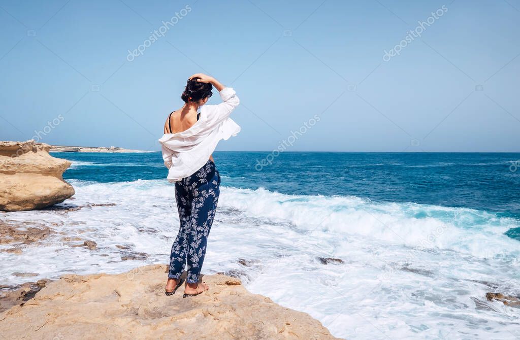 Woman in light clothing stay on windy sea coast