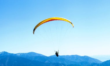 Mavi dağların üzerinden gökyüzünde süzülen paraglider 