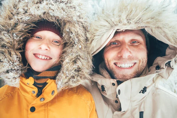 父亲和儿子穿着保暖帽衫和便衣在雪地的森林里散步 脸上挂着笑脸的画像 父子关系与冬装概念形象 — 图库照片