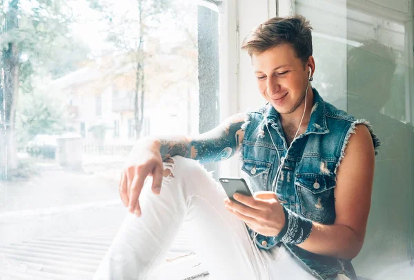 Joven Escuchar Música Con Auriculares Teléfono Inteligente Sentado Alféizar Ventana — Foto de Stock