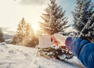 Eldivenli bir adam, bir fincan sıcak çay ve kar ormanı arkaplanlı.