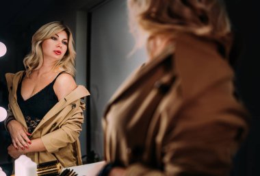 Orta yaşlı, baştan çıkarıcı kadının yansımasına bakıp Trench ceketinin altındaki iç çamaşırının değerini anlayan şehvetli portresi. İnsani duygular ya da kıyafet moda imajı.