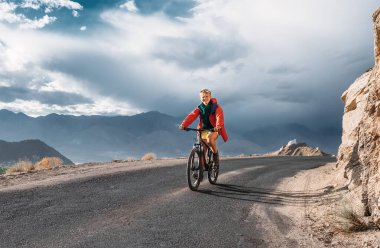 Genç adam Himalaya Dağı 'nda bisiklet sürüyor. Fırtına gökyüzü arkaplanı