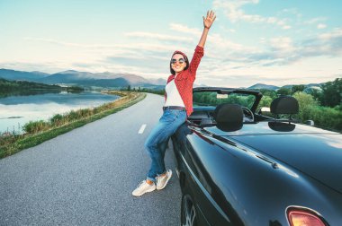 Gülümseyen mutlu genç kadın dağ yolunda Cabriolet arabasının yanında kal.