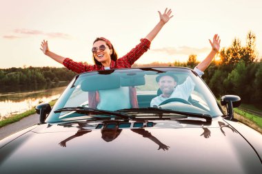 Arabayla seyahat etmek - aşık mutlu bir çift gün batımında Cabriolet arabasıyla gider