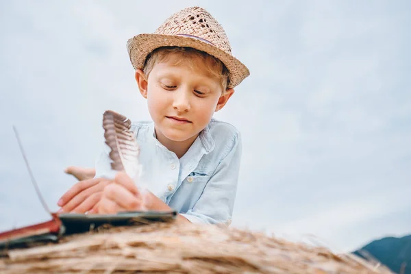 男の子は干し草のロールに横たわる羽のノートを書きます — ストック写真