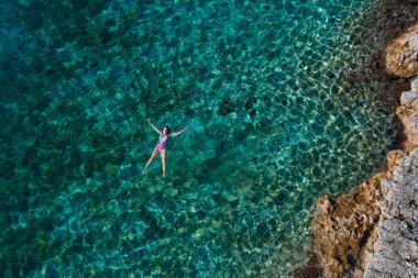 Genç bir dişi arkada yüzüyor ve Adriyatik 'in sıcak turkuaz deniz dalgalarında kayalık sahil şeridinde dinleniyor. Tasasız insanlar tatil zamanı konsepti gökyüzü görüntüsü.
